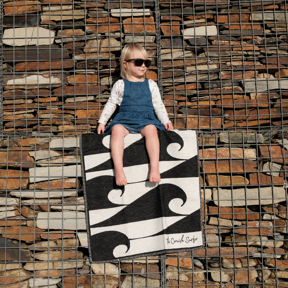 Child sitting on a black and white patterned rug against a stone wall.