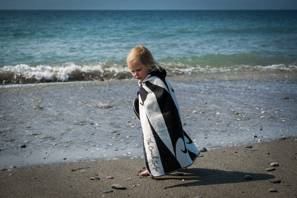 Person wearing a black and white patterned blanket on a beach with ocean waves in the background