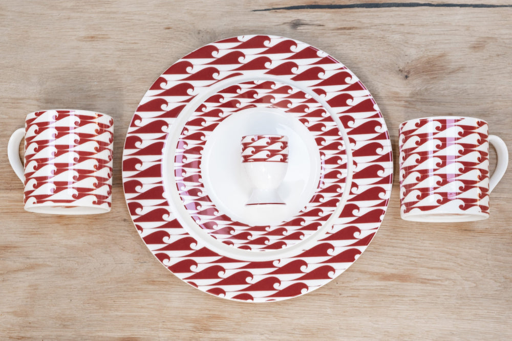 Set of red and white patterned ceramic plates and mugs on a wooden surface