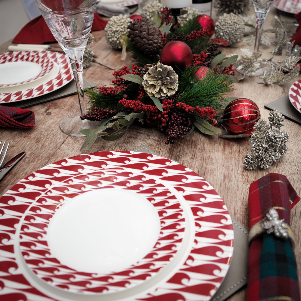 Decorative Christmas table setting with red and white patterned plates, greenery, and ornaments.