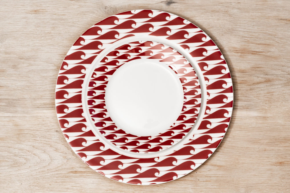 Set of ceramic plates with red and white wave pattern on a wooden surface