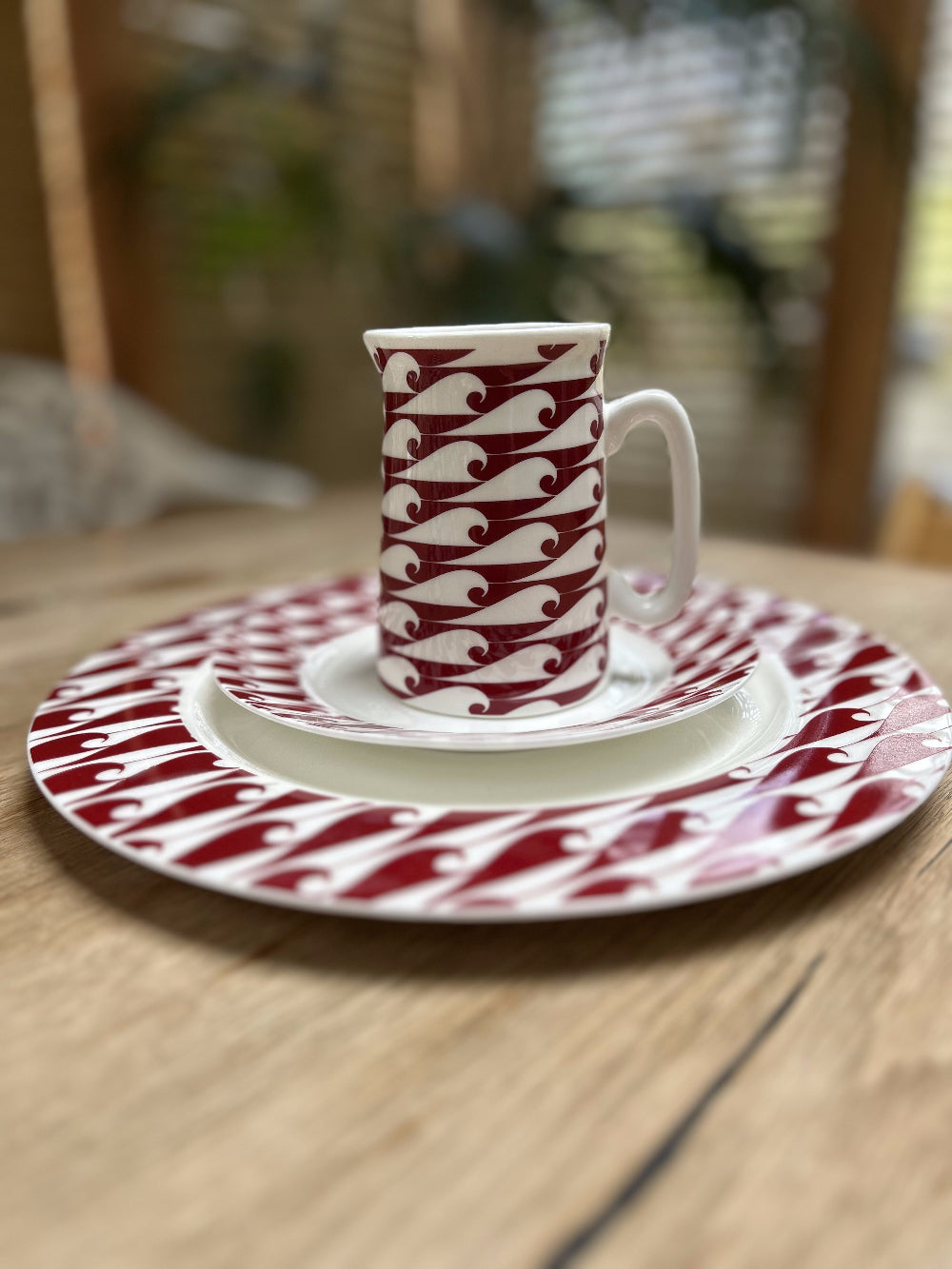 Red and white patterned cup and saucer set on a matching plate on a wooden table.