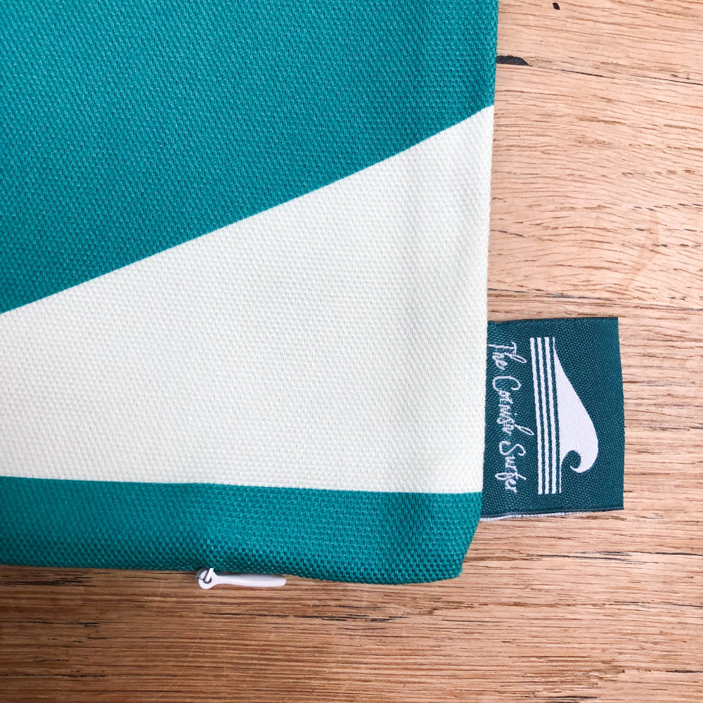 Teal and white striped cushion cover with The Cornish Surfer brand tag on a wooden surface