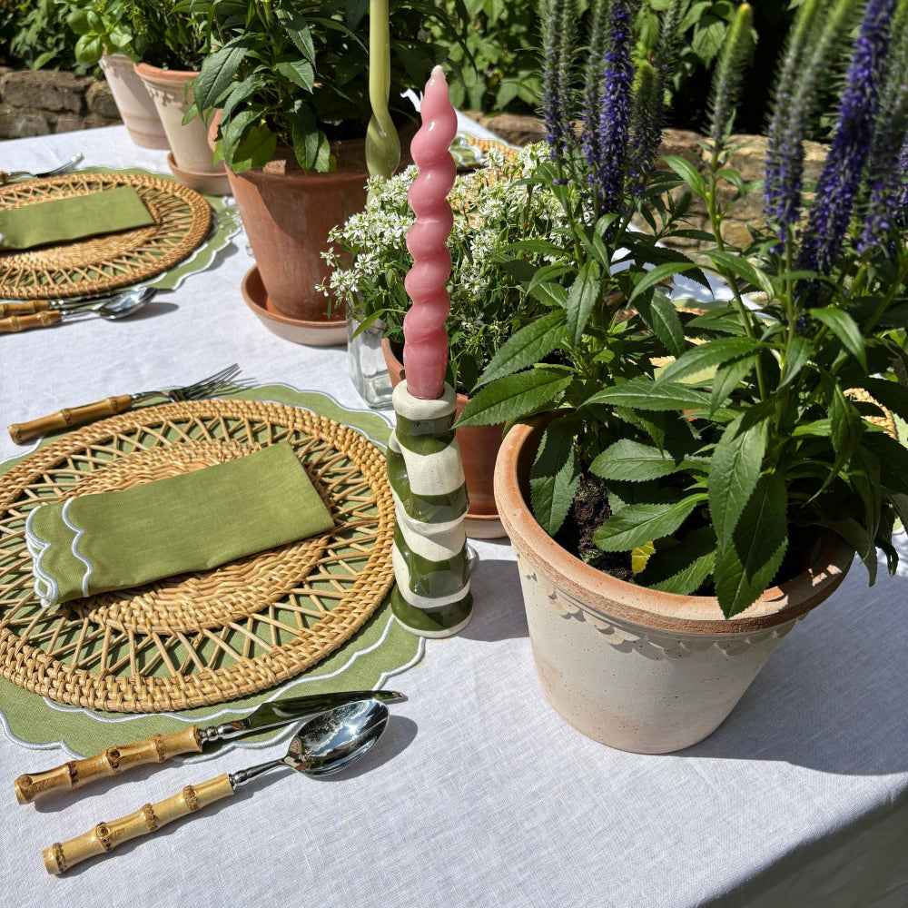 Outdoor table setting with woven placemats, green napkins, and potted plants.