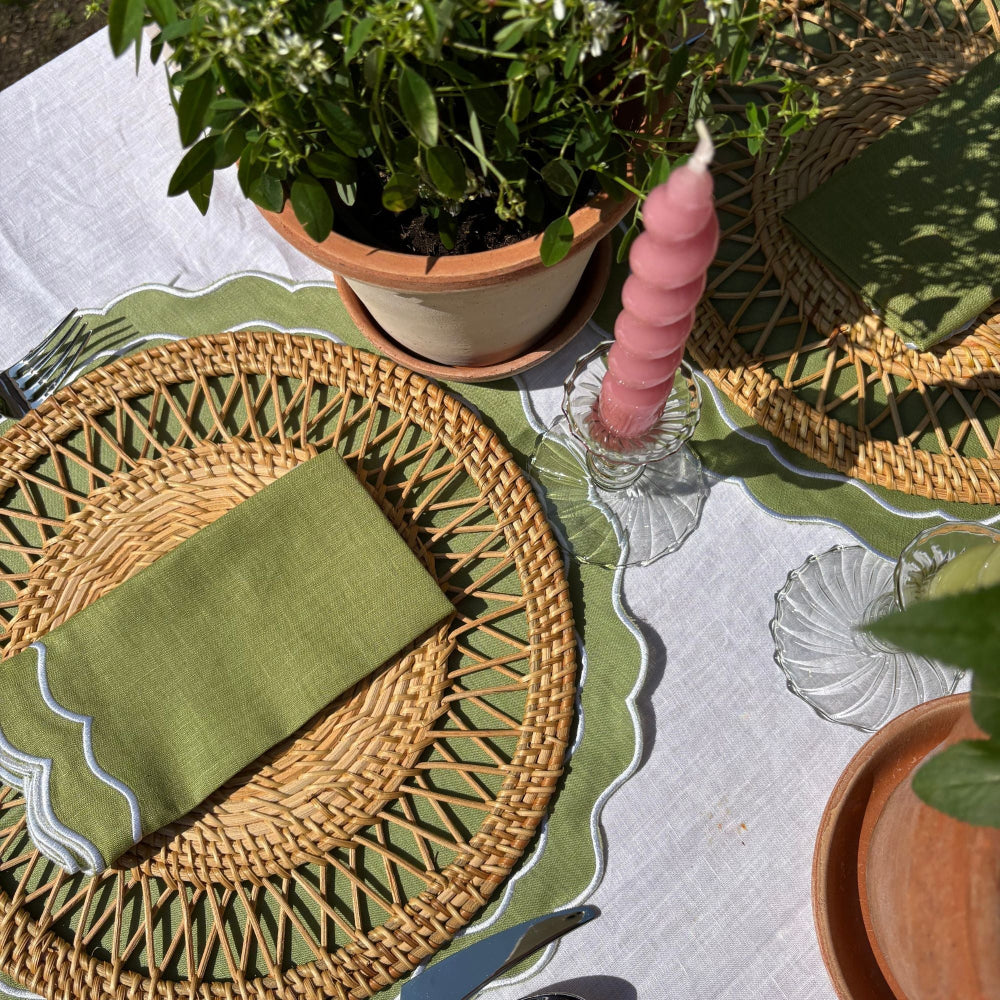 Table setting with woven placemats, green napkins, and a pink candle.
