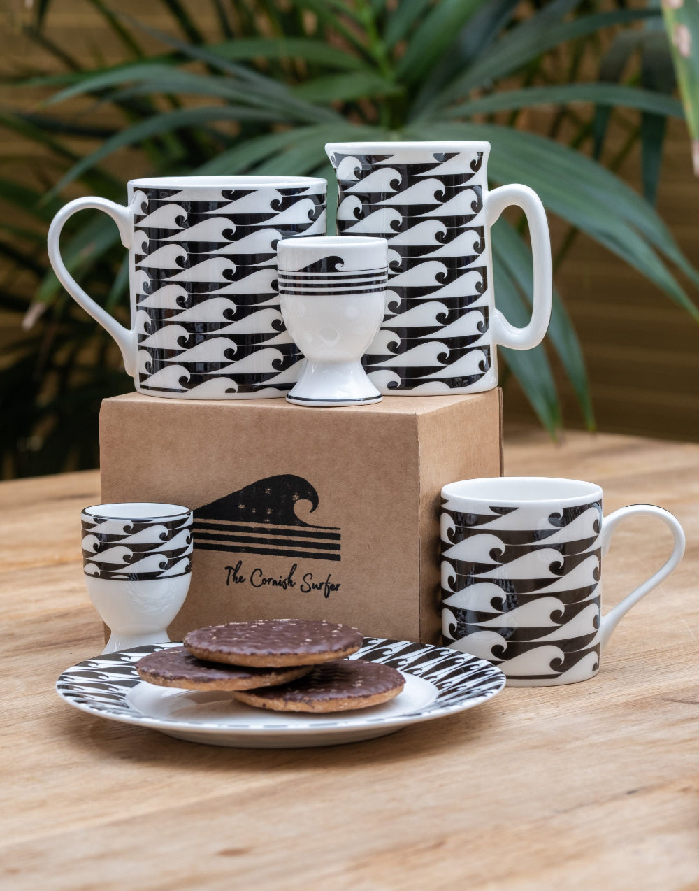 Set of black and white patterned ceramic items on a wooden surface with a plant in the background.
