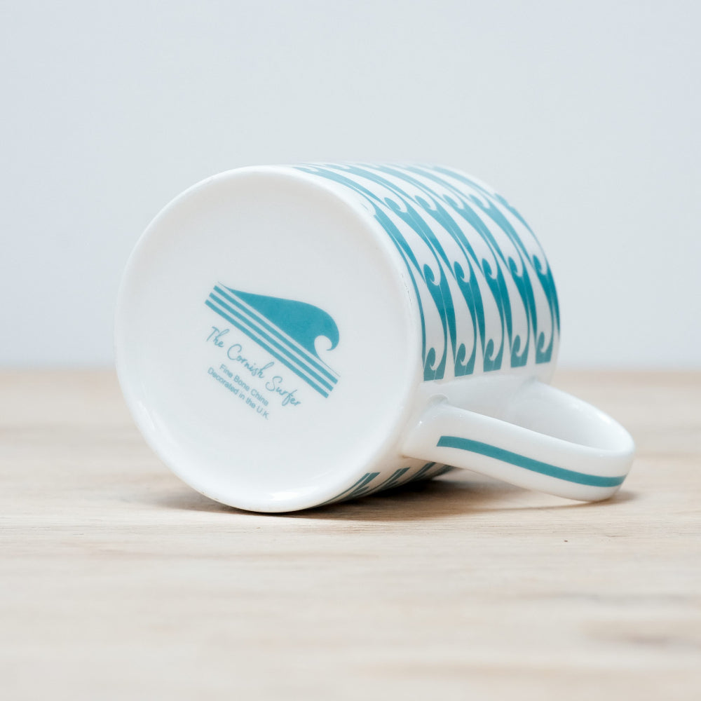 White mug on side with blue wave design on a wooden surface