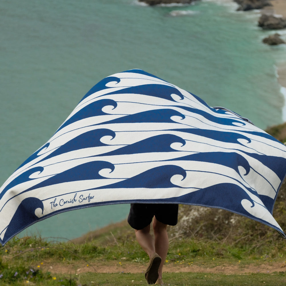 Person holding a blue and white wave-patterned towel with a coastal background