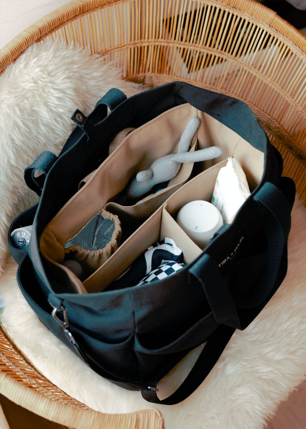Black diaper bag with compartments on a fluffy white surface