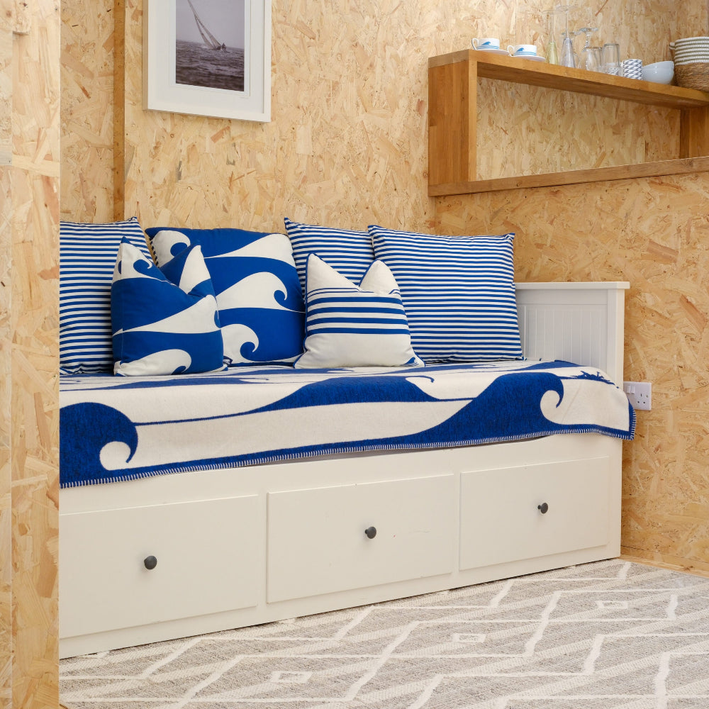 White bench with blue and white wave-patterned cover and pillows against a wooden wall.