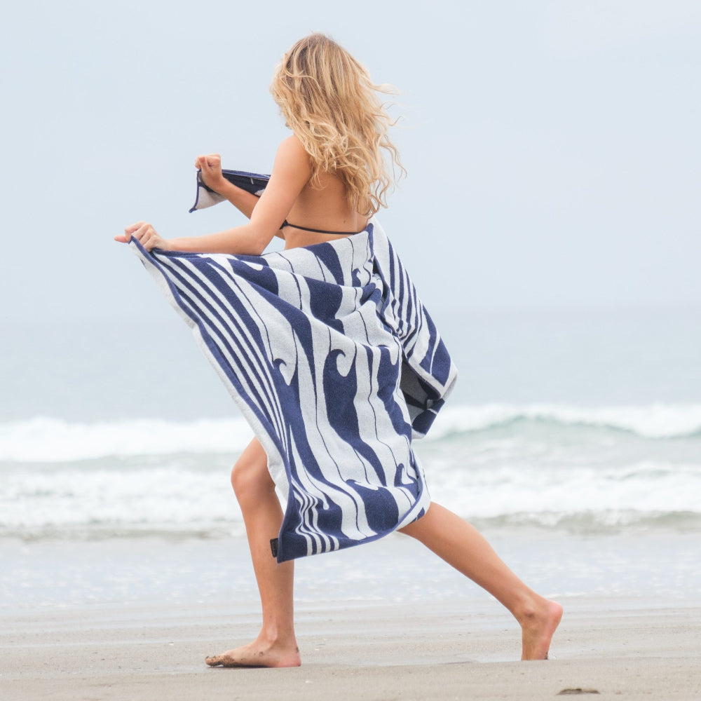 Woman on a beach holding a blue and white patterned towel