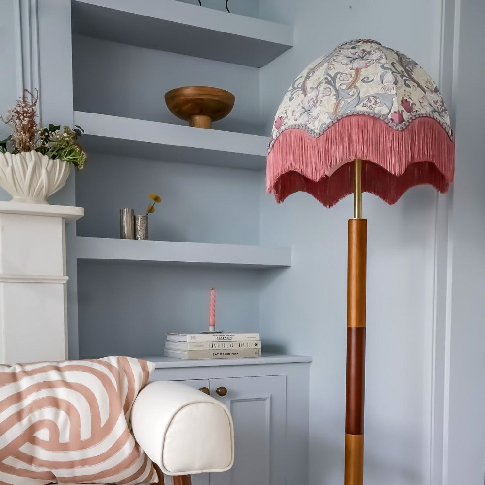 Decorative lamp with a floral shade in a room with shelves and a chair.