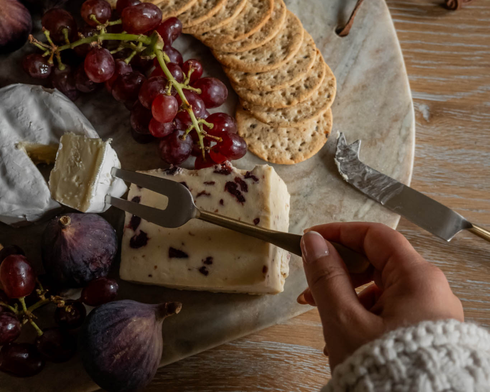 Cheeseboard with assorted cheeses, crackers, grapes, and figs on a wooden board.
