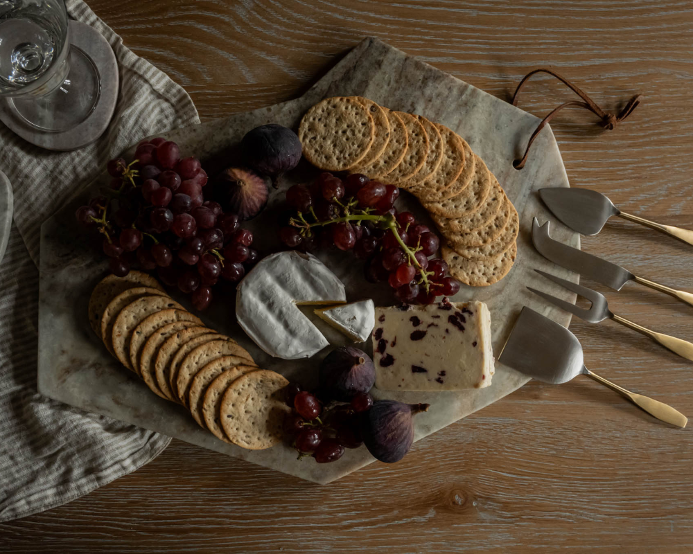 Platter of assorted cheeses, crackers, and fruits on a wooden table with cheese knives.