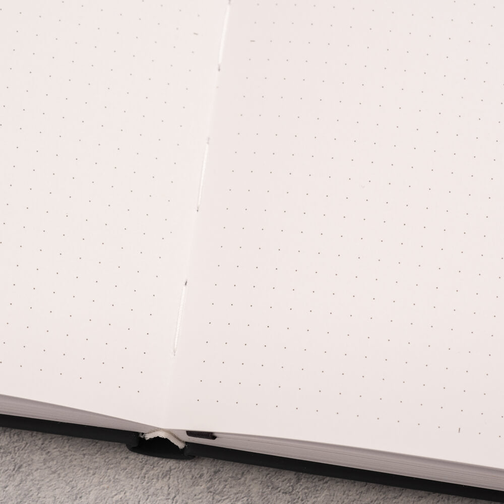 Close-up of a white notebook with black binding on a light grey surface.