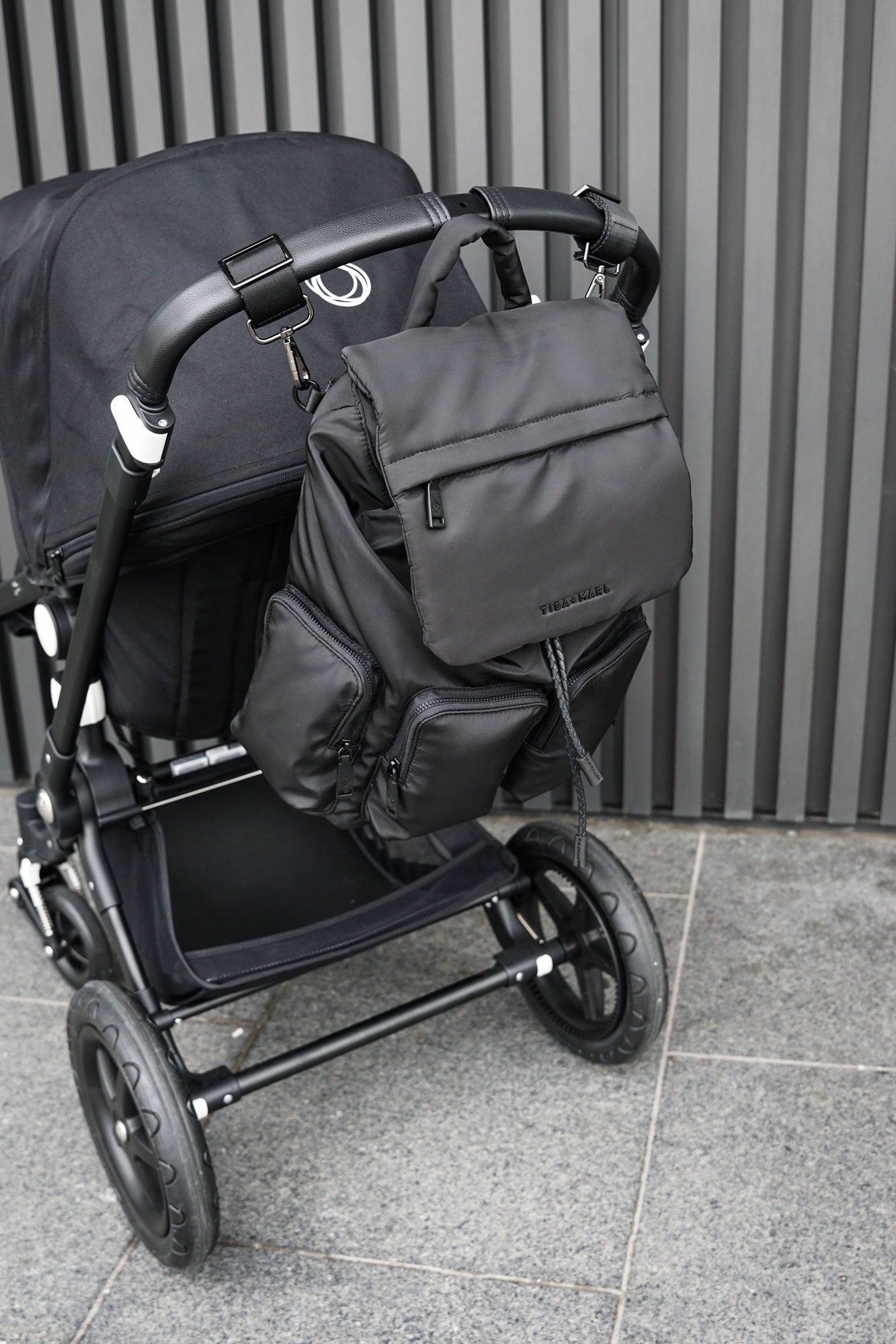 Black stroller with a matching backpack against a gray wall.