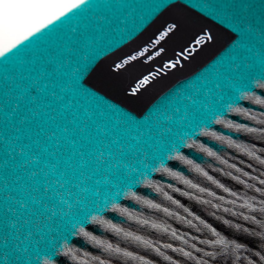 Teal scarf with grey fringe and a brand label on a white background
