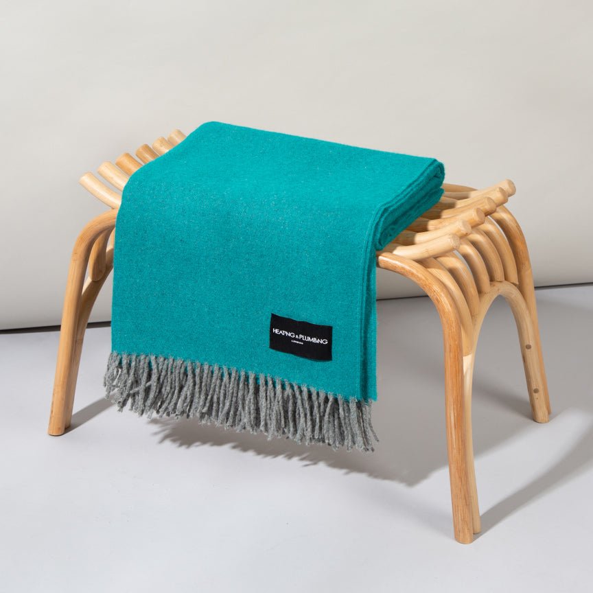 Turquoise blanket with a brand label draped over a wooden stool on a light grey background
