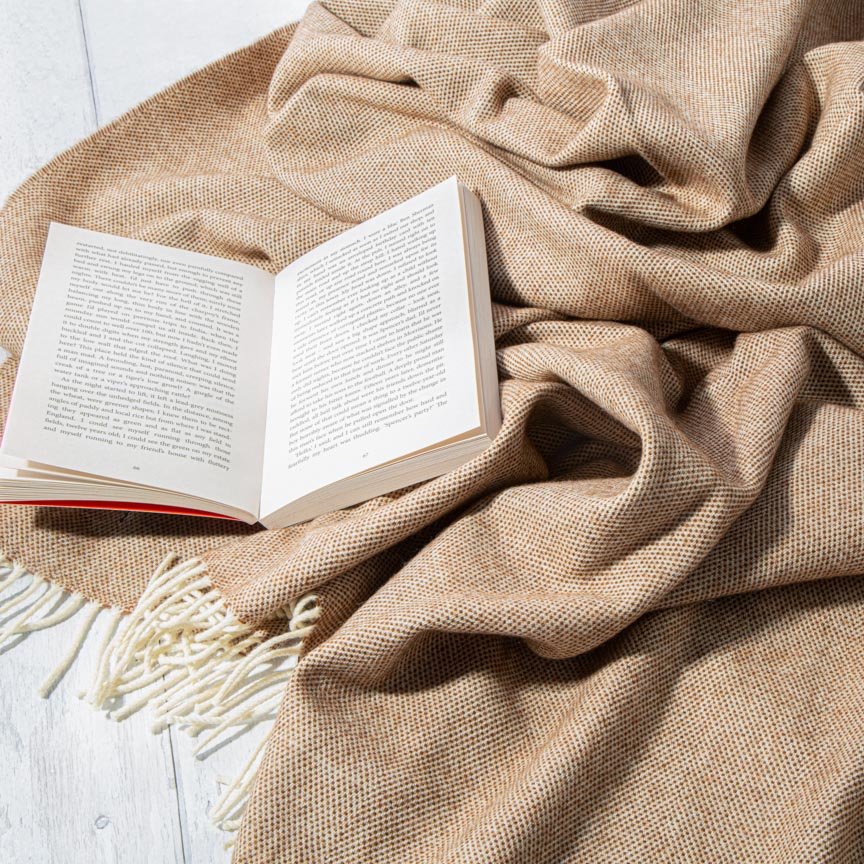 Open book on a beige blanket with tassels on a light wooden surface