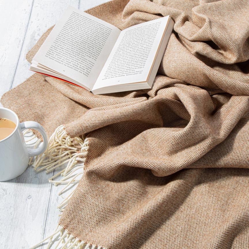 Open book and mug of coffee on a beige blanket on a light wooden surface