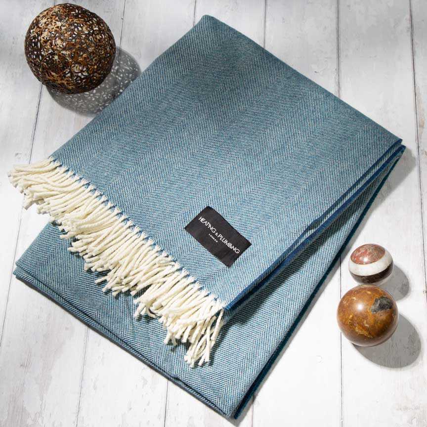 Blue throw blanket with white fringe on a light wooden floor