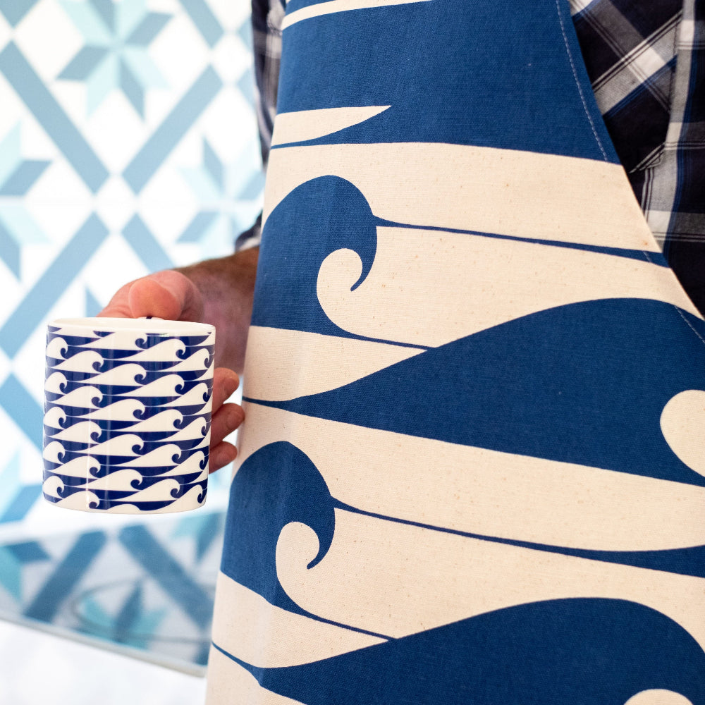 Person wearing a blue and white wave-patterned apron holding a matching mug.