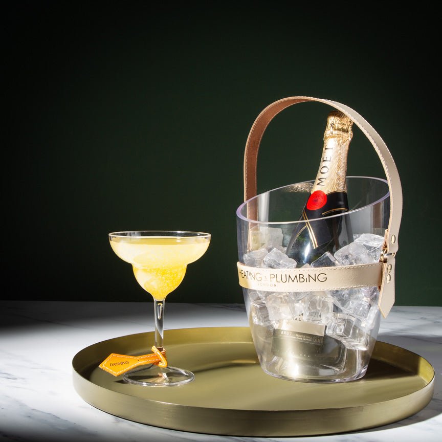 Mojito cocktail in a glass with a bottle of Moet champagne in an ice bucket on a gold tray.