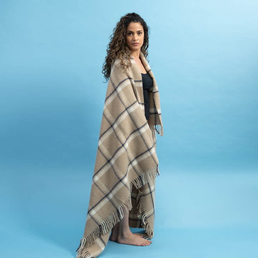 Woman wearing a beige plaid blanket against a blue background