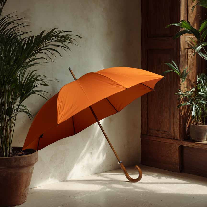 Orange umbrella leaning against a wall with plants around