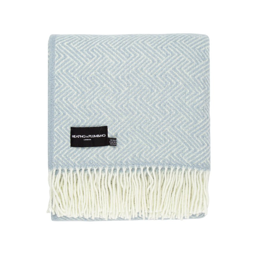 Duck egg coloured woven blanket with a white fringe and a black label on a white background