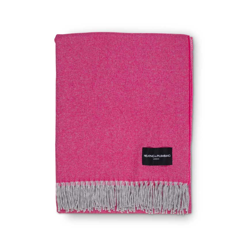 Pink throw blanket with grey fringe and a brand label on a white background folded