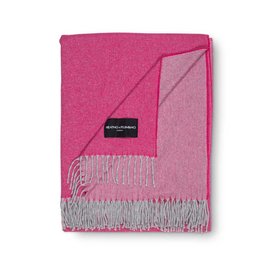 Pink throw blanket with grey fringes folded and a brand label on a white background