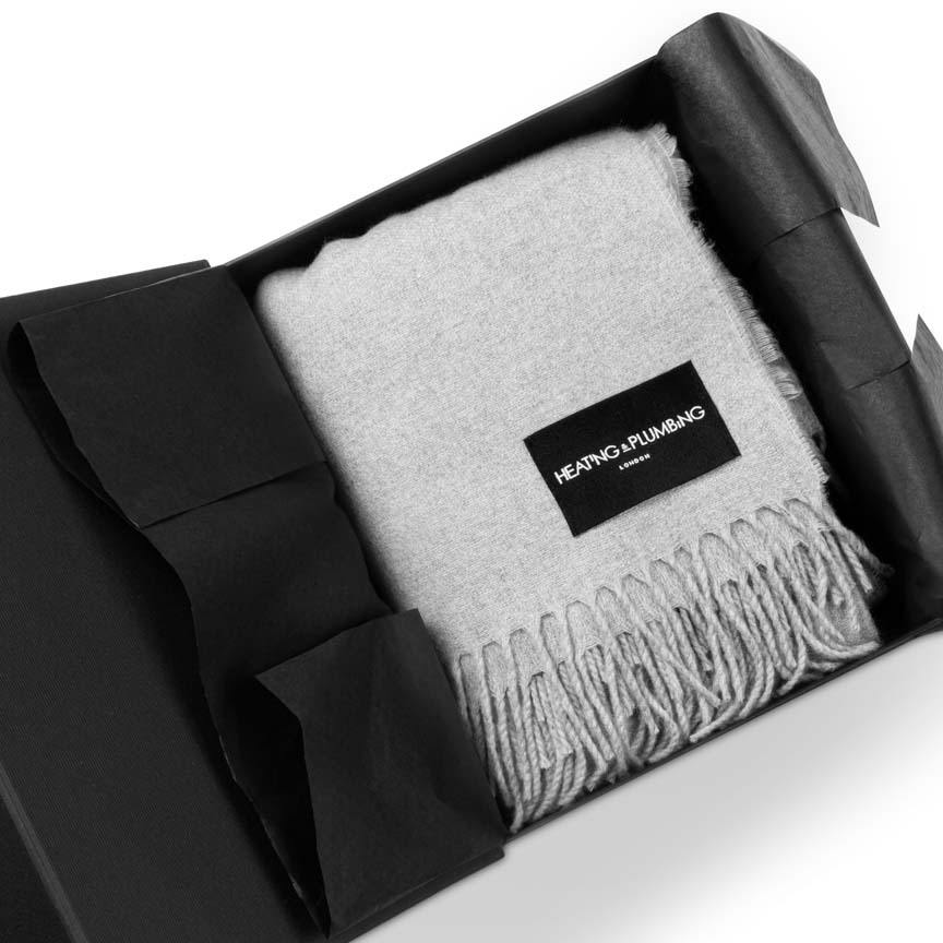 Grey blanket with a brand label Heating and Plumbing in an open black box on a white background