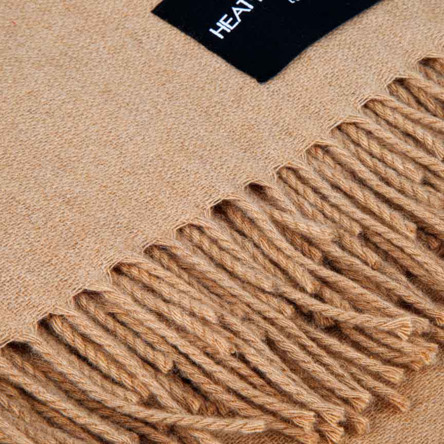 Close-up of a beige blanket with fringes and a brand label.