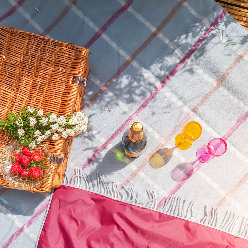 Picnic setup with a wicker basket, flowers, and drinks on a checkered blanket.