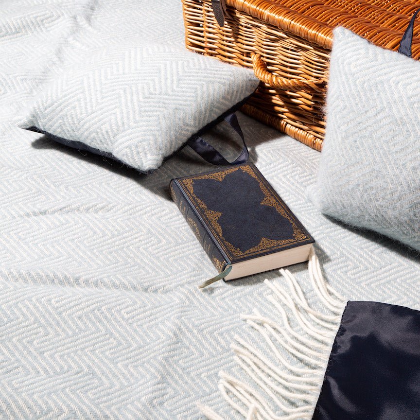 Vintage book on a textured blue blanket with wicker basket and pillows in the background