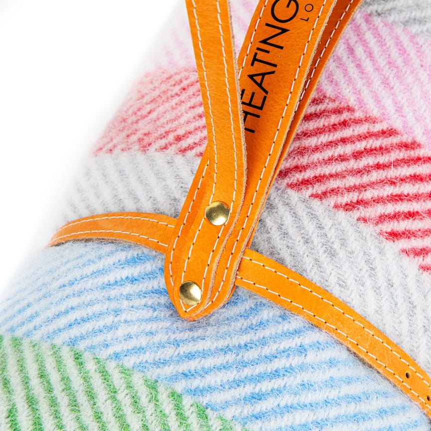 Close-up of a colourful blanket with an orange strap and visible brand name.