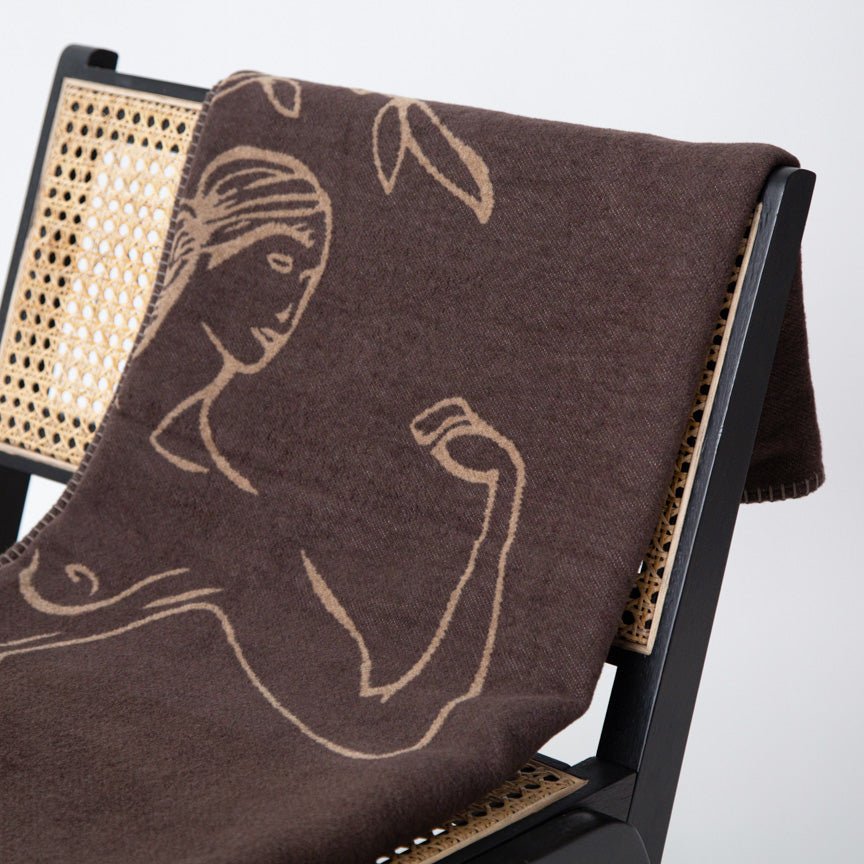 Brown blanket with beige embroidery of a woman on a chair