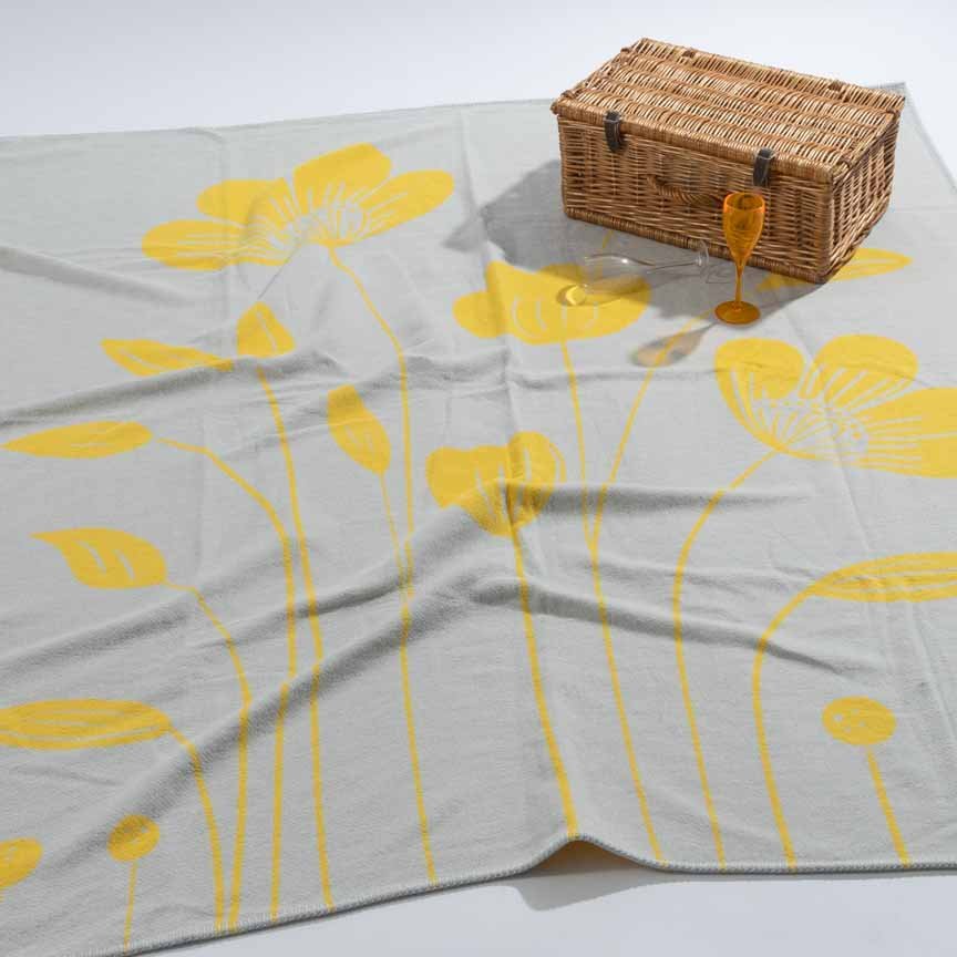 Grey blanket with yellow floral patterns on a white surface, accompanied by a wicker picnic basket and glasses.