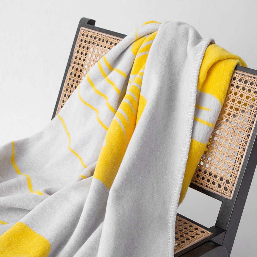 Grey and yellow blanket draped over a chair with a white background