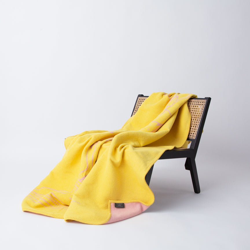 Yellow blanket draped over a black wicker chair on a white background