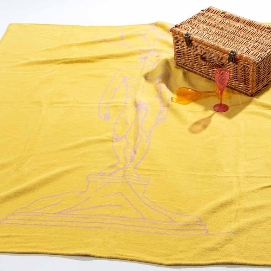 Yellow blanket with a picnic setup including a wicker basket and glasses on a white background