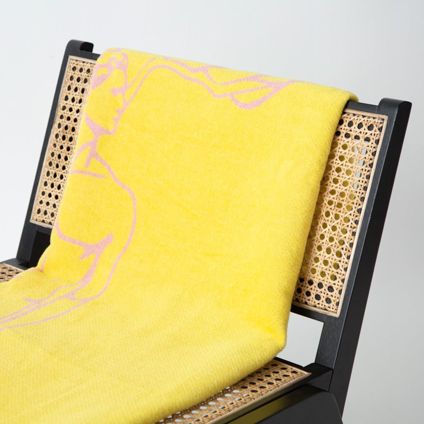 Yellow blanket with pink design draped over a wicker chair against a grey background