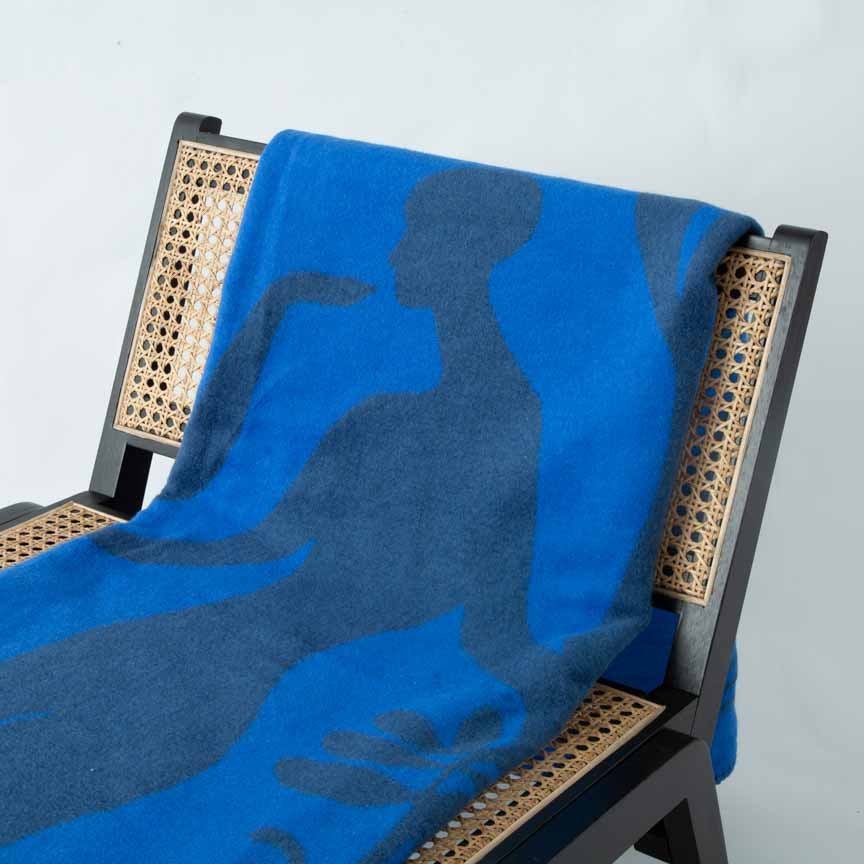 Blue towel draped over a chair with a wicker backrest on a light grey background