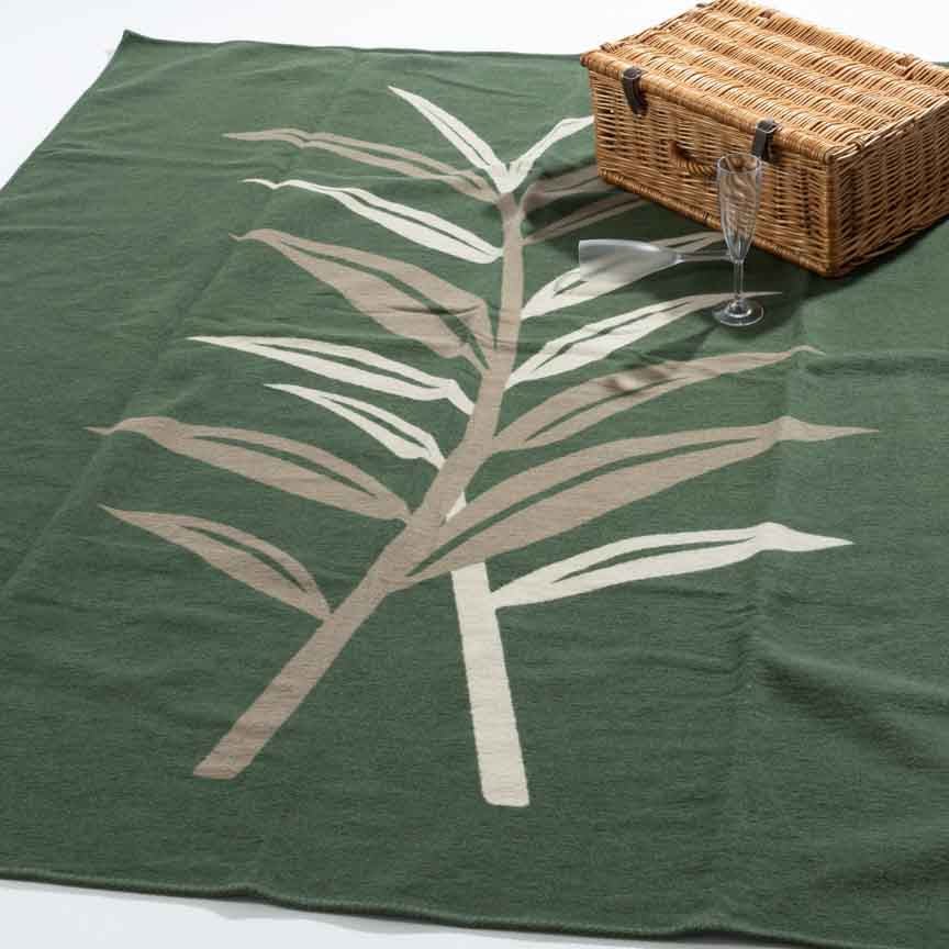 Green blanket with white leaf design and picnic basket on a white background
