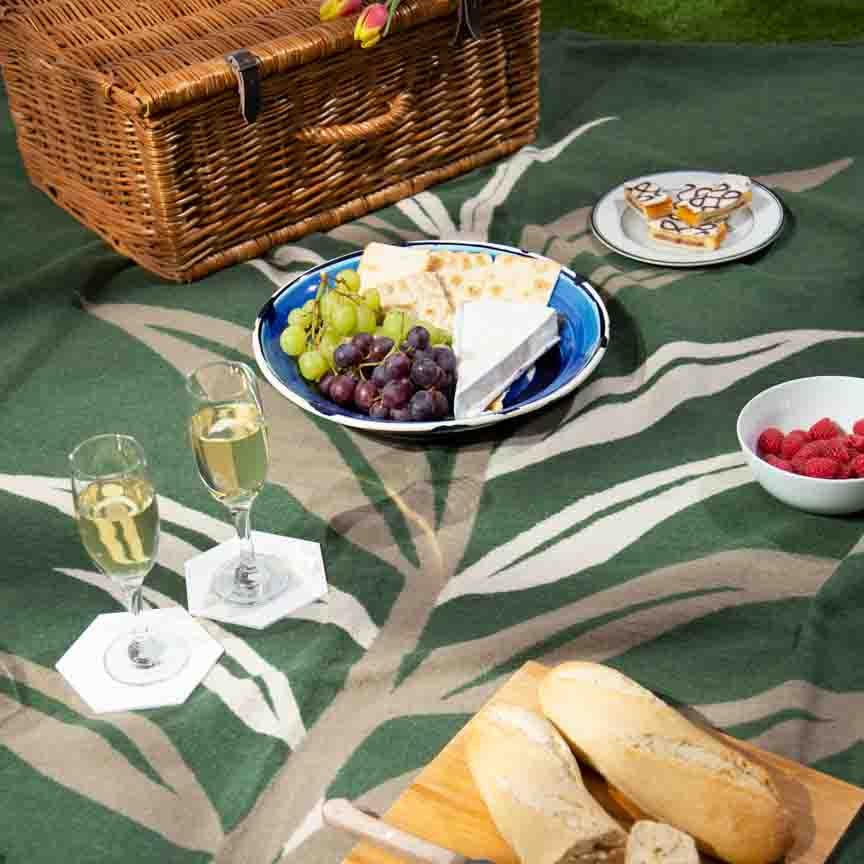 Picnic setup with bread, cheese, fruits, and wine on a green patterned blanket.