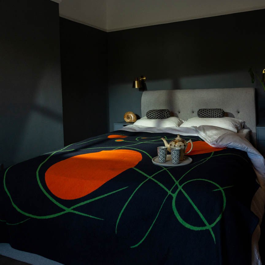 Bed with a decorative blanket orange and black featuring orange and green shapes in a dimly lit room.