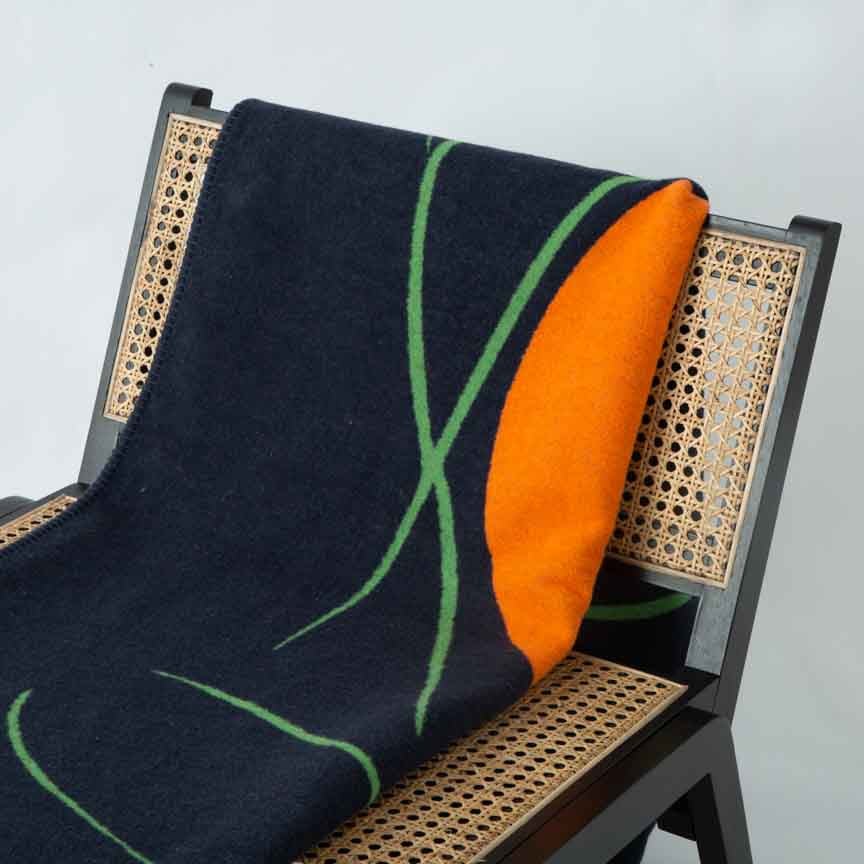 Black recycled blanket with green and orange design draped over a chair with a wicker backrest.