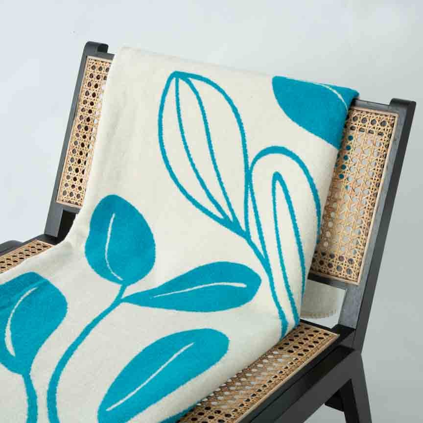 Teal leaf-patterned blanket draped over a wicker chair against a light grey background