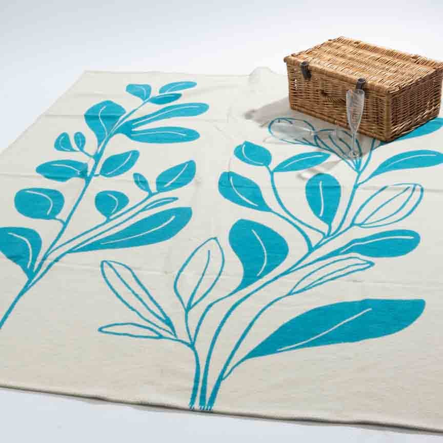 Blanket with blue leaf design on a white background with picnic basket and wine glass